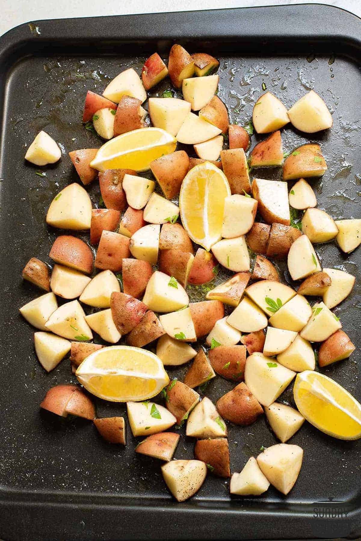 the chopped potatoes and lemons on a baking tray