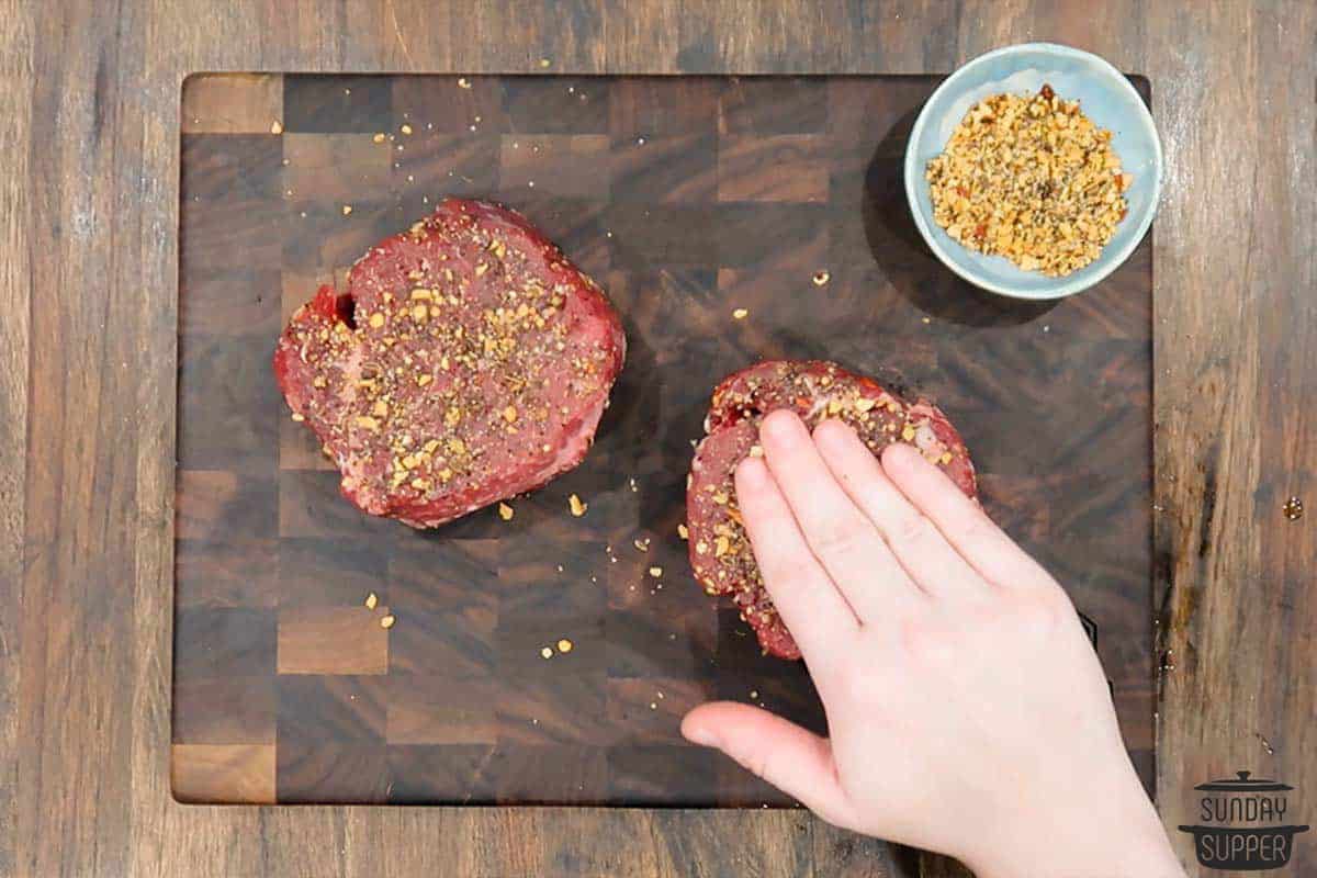 seasoning being patted down on two filet mignon steaks