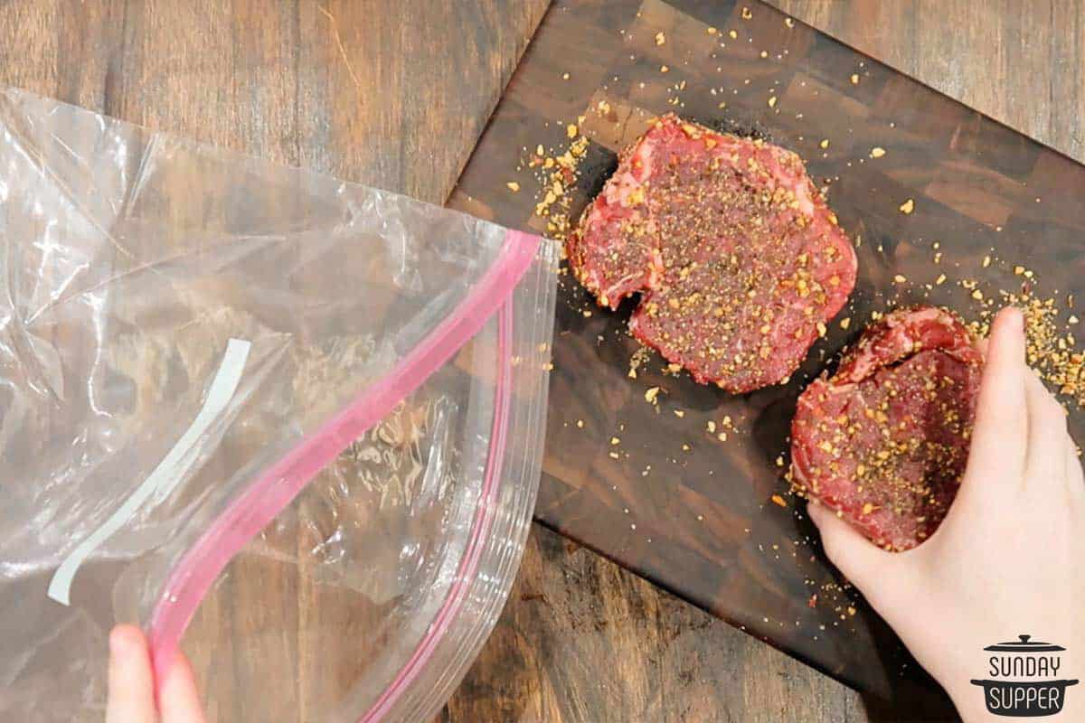 seasoned steaks being placed in a ziplock bag
